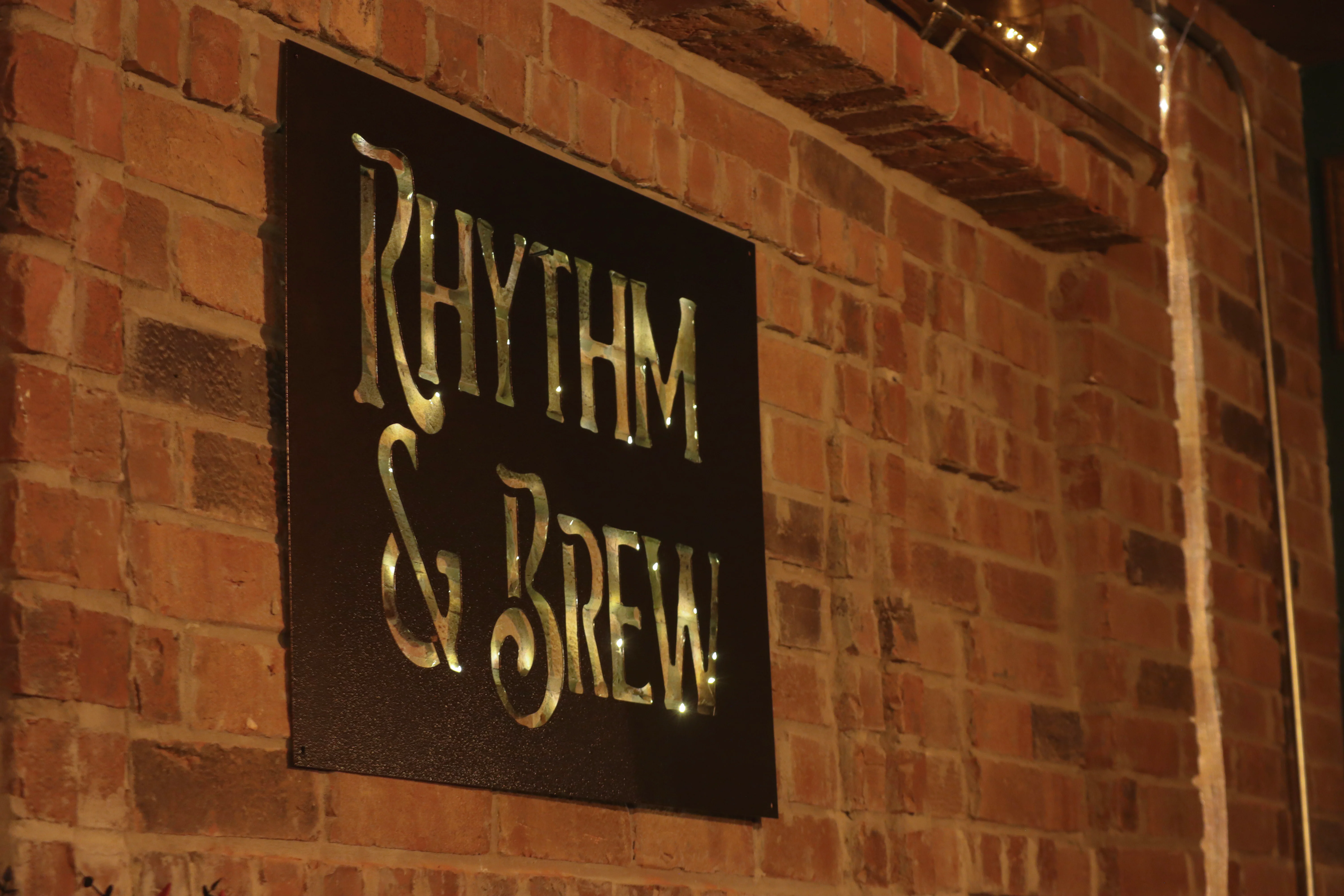 Illuminated Rhythm & Brew sign on the brick wall